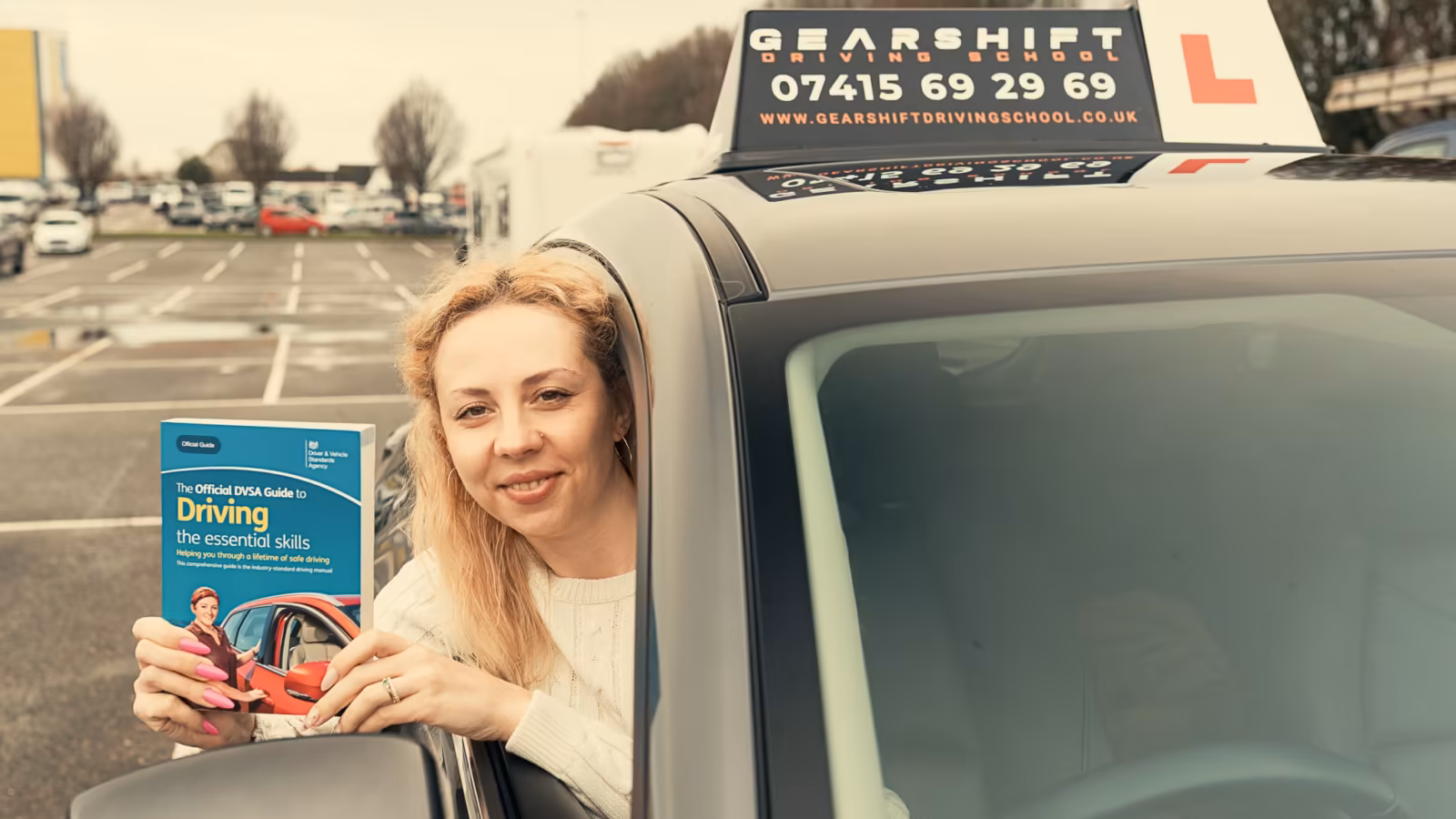 Learner smiling from the Gearshift car window holding the DVSA driving guide
