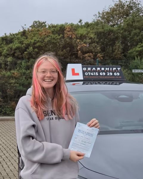 Learner holding their driving test pass certificate next to the Gearshift Driving School car
