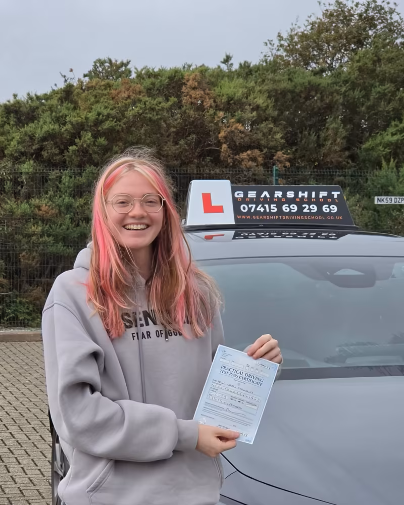 Learner holding their driving test pass certificate next to the Gearshift Driving School car