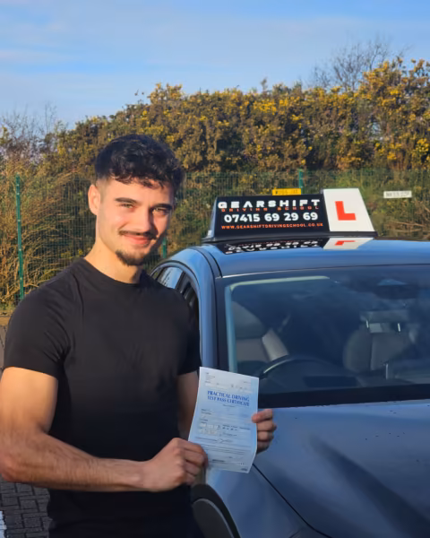 Learner holding their driving test pass certificate next to the Gearshift Driving School car