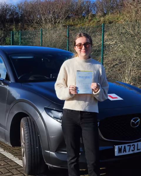 Learner holding their driving test pass certificate next to the Gearshift Driving School car
