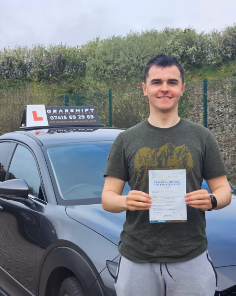 Learner holding their driving test pass certificate next to the Gearshift Driving School car