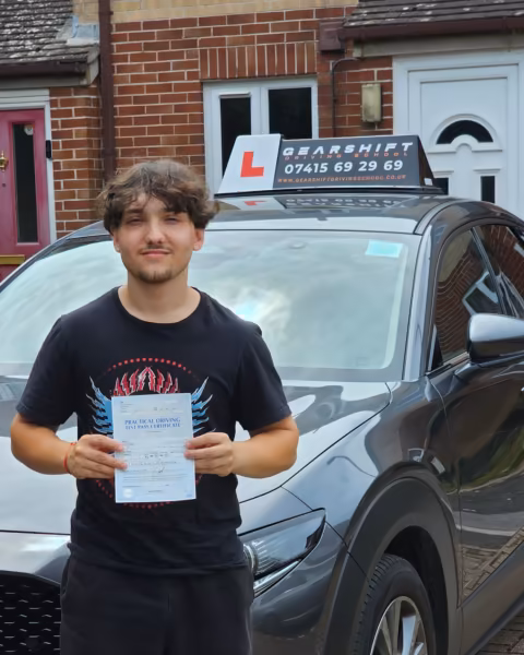 Learner holding their driving test pass certificate next to the Gearshift Driving School car