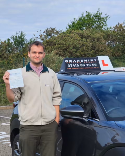 Learner holding their driving test pass certificate next to the Gearshift Driving School car