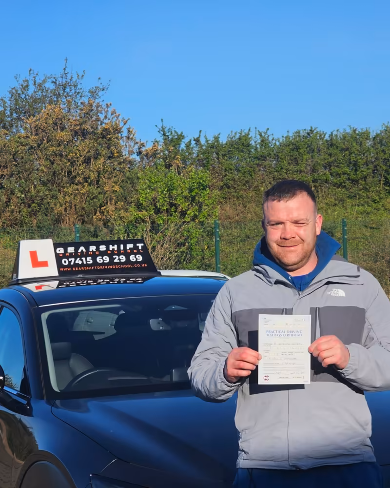 Learner holding their driving test pass certificate next to the Gearshift Driving School car