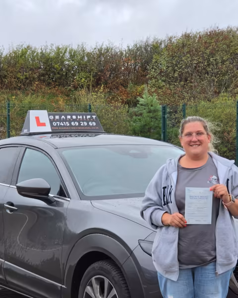 Learner holding their driving test pass certificate next to the Gearshift Driving School car
