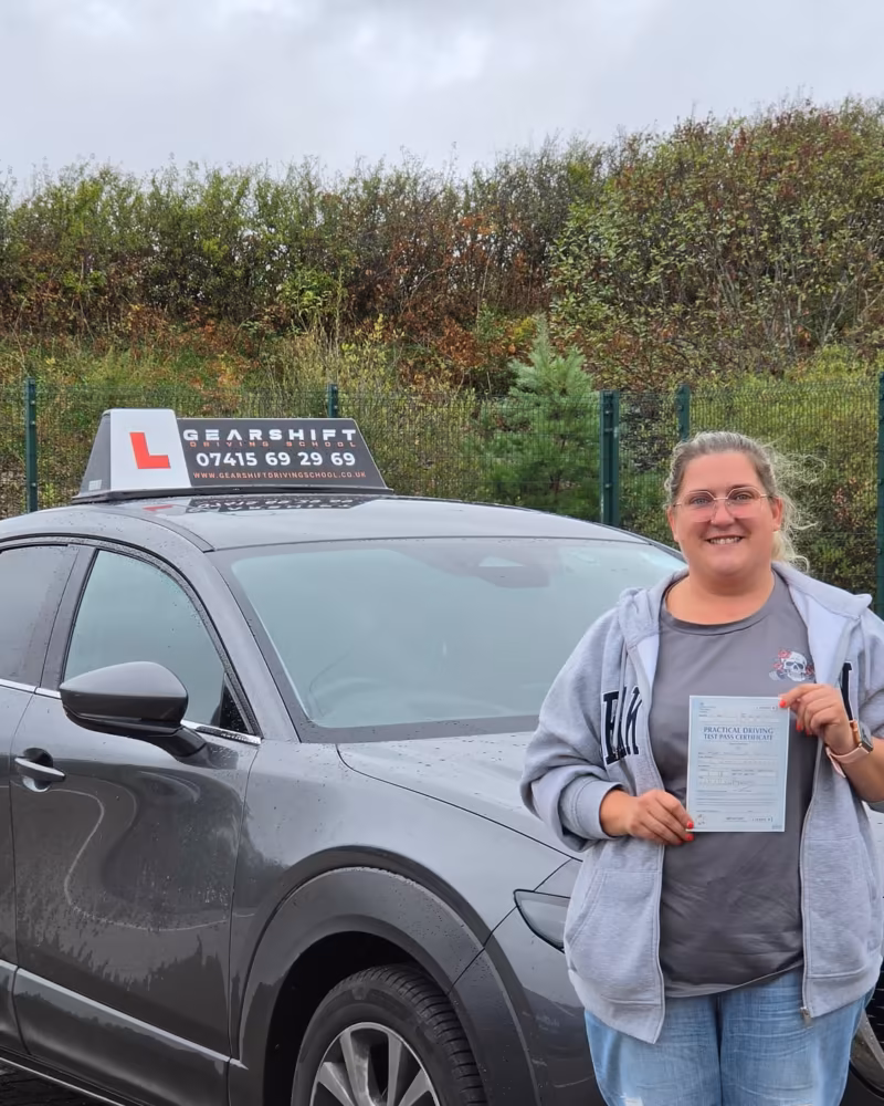 Learner holding their driving test pass certificate next to the Gearshift Driving School car