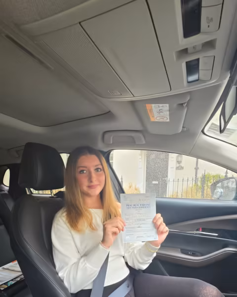 Learner holding their driving test pass certificate next to the Gearshift Driving School car
