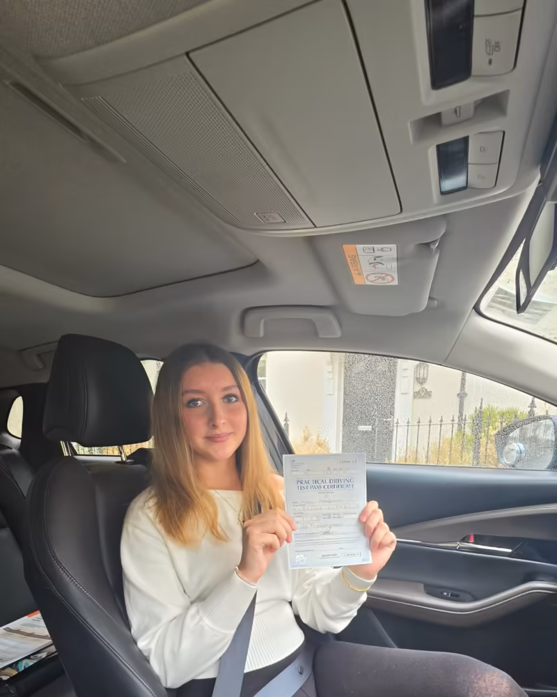 Learner holding their driving test pass certificate next to the Gearshift Driving School car